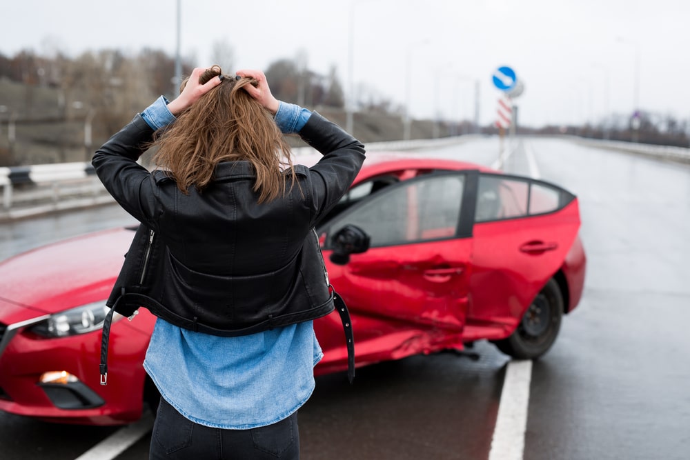 woman stands near broken car after hurricane related accident - Legal Implications of Hurricane-Related Car Accidents