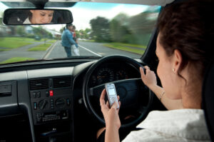  A woman texting while driving, unaware of a mother and child crossing the road, illustrating the critical dangers of distracted driving.
